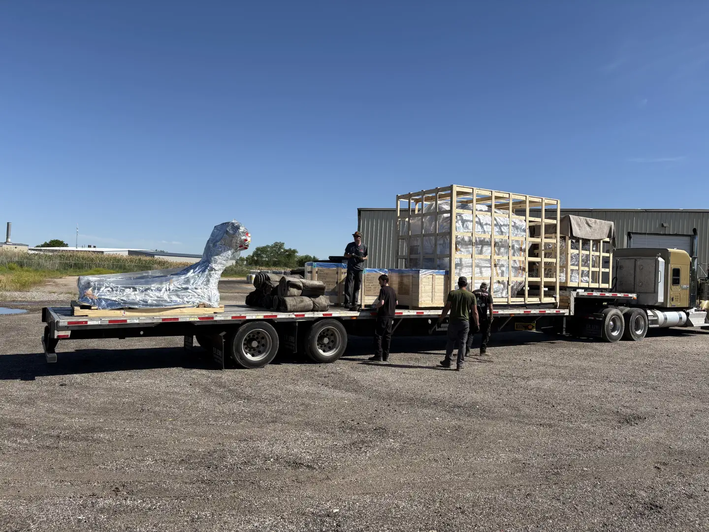 Flatbed truck loading large crated items and wrapped machinery.