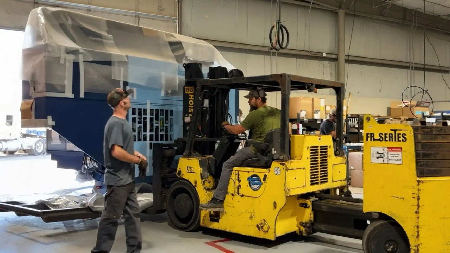 Forklift moving a large, blue, covered object in a warehouse.